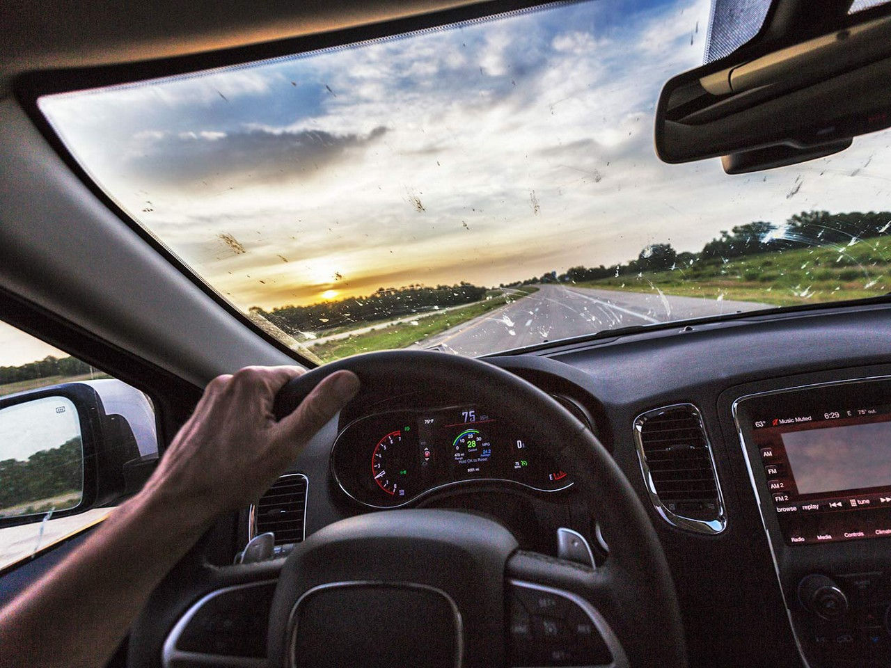 A close-up view of a person driving and the car windshield is covered in bug splatter.