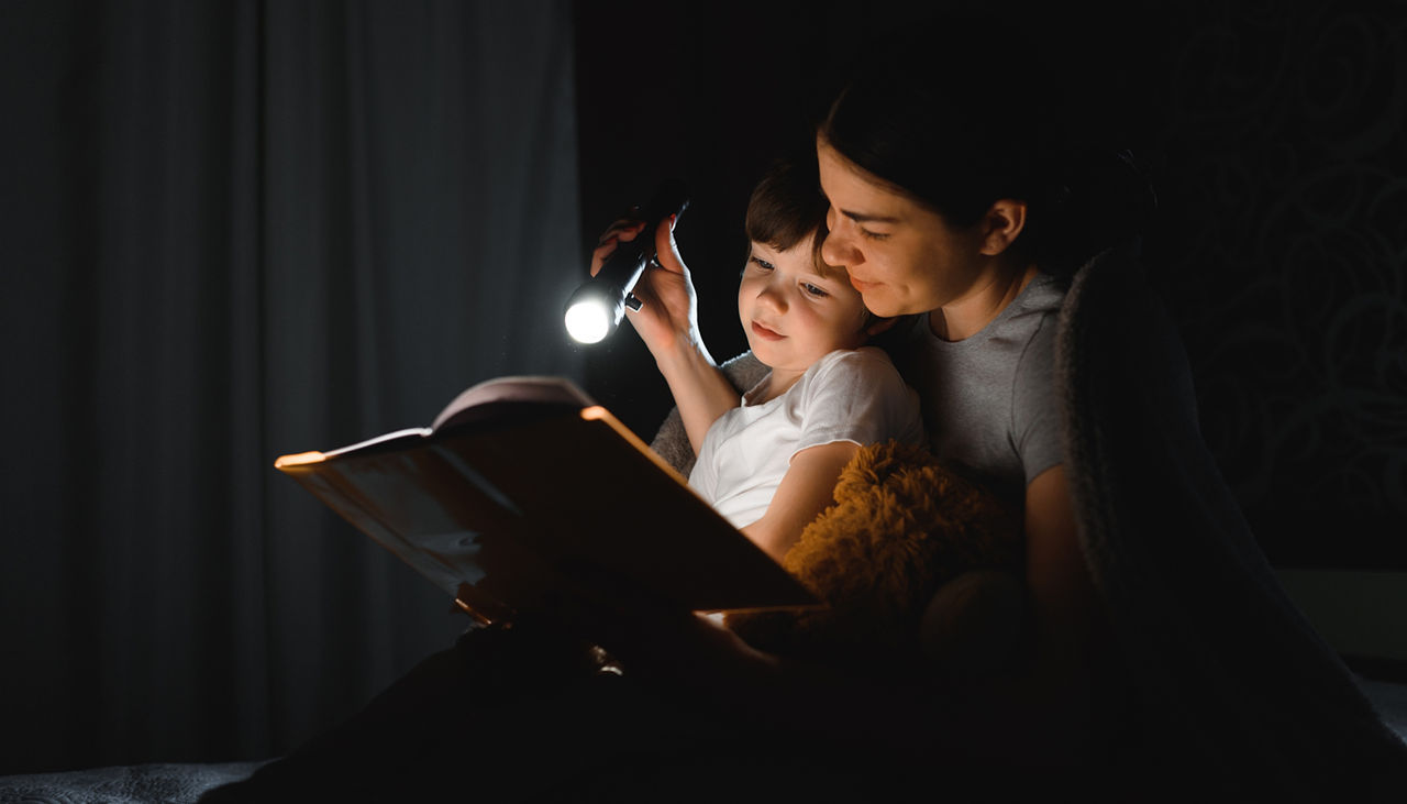 Mother and son reading a book with a flashlight during a power outage