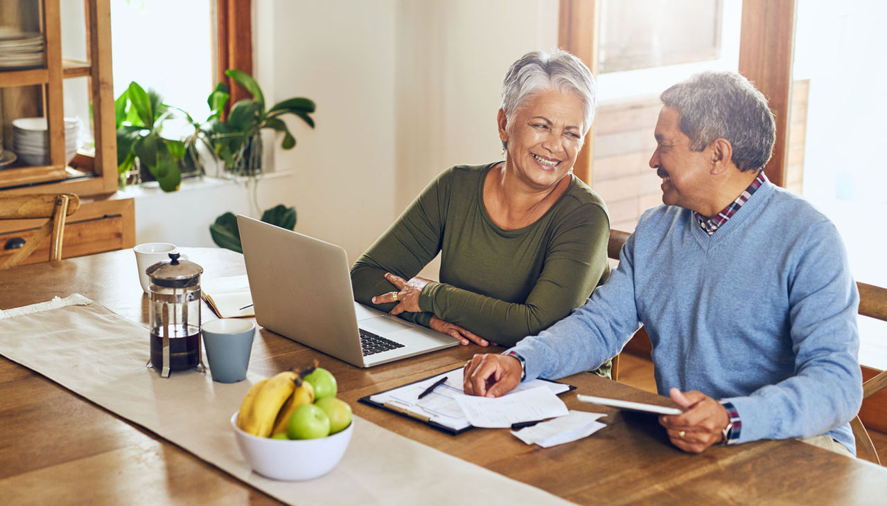 Happy senior couple at home, going over finances on laptop